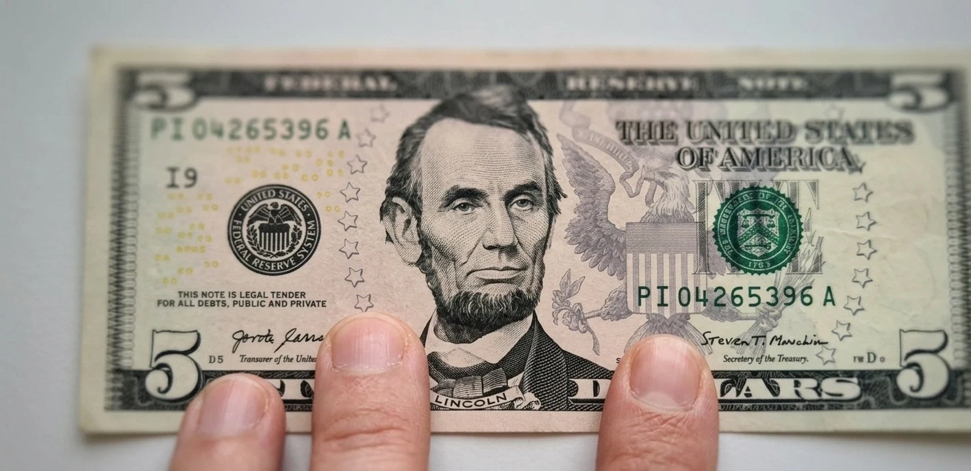 an Abraham Lincoln 5 dollar bill held flat by fingers